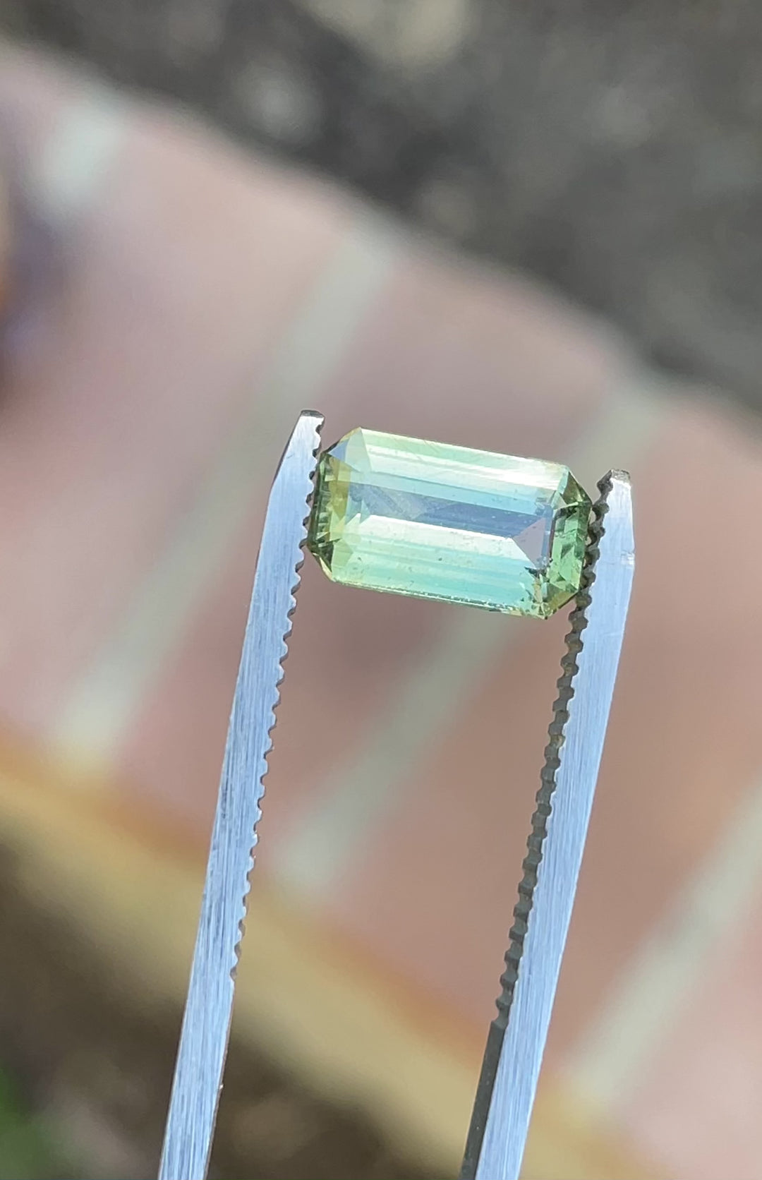 Video spinning a 2.24-carat modified emerald cut sapphire with yellow, teal, and green colors under natural light.