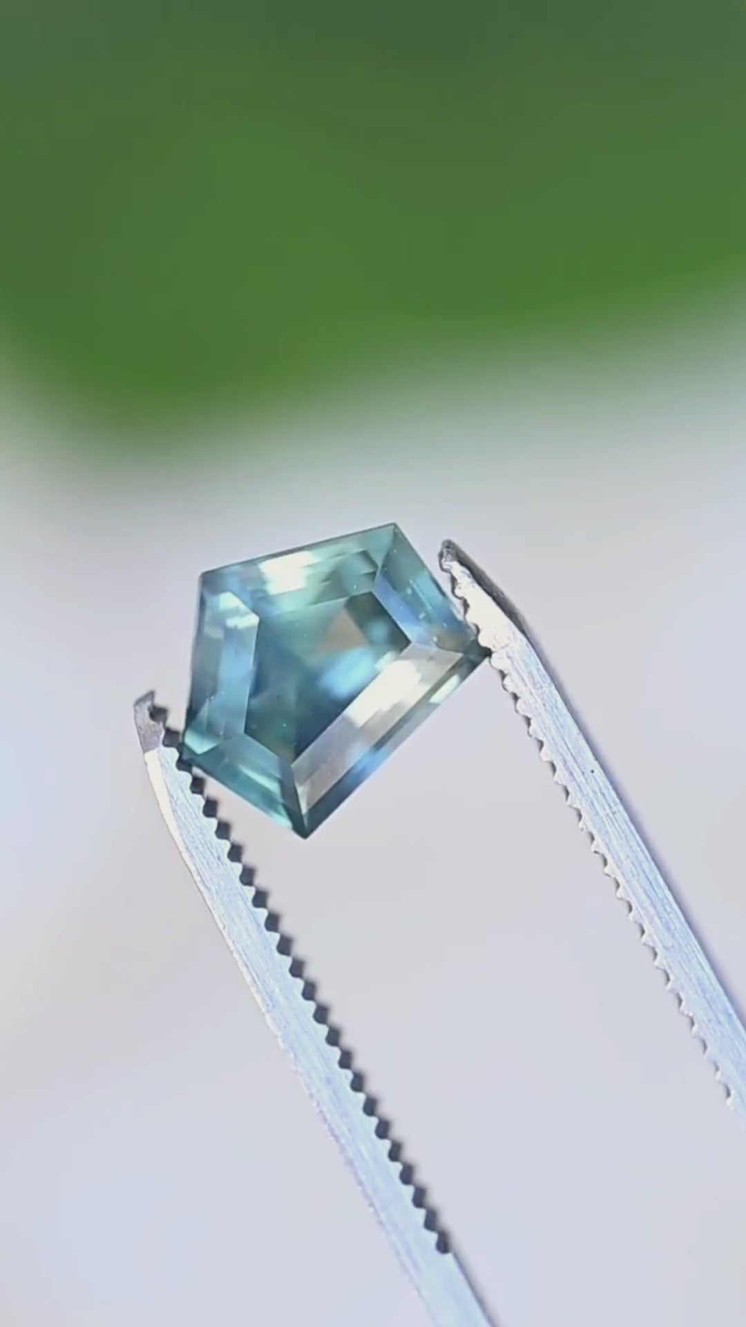 Explore the shifting blue and green tones of this 3.54ct heated sapphire from Diego, Madagascar. Filmed in gem tweezers, its custom shield step cut reveals geometric reflections, bright aquatic blue flashes, and deeper teal tones as the viewing angle changes. A distinctive loose sapphire for custom engagement rings and bespoke fine jewelry.
