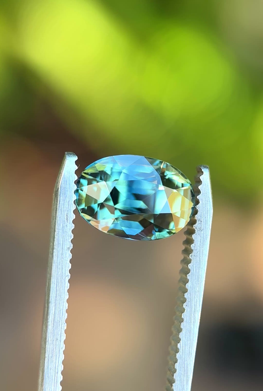 4.24ct parti green teal blue sapphire rotating in hand, revealing dramatic color zoning and bright precision-cut reflections.