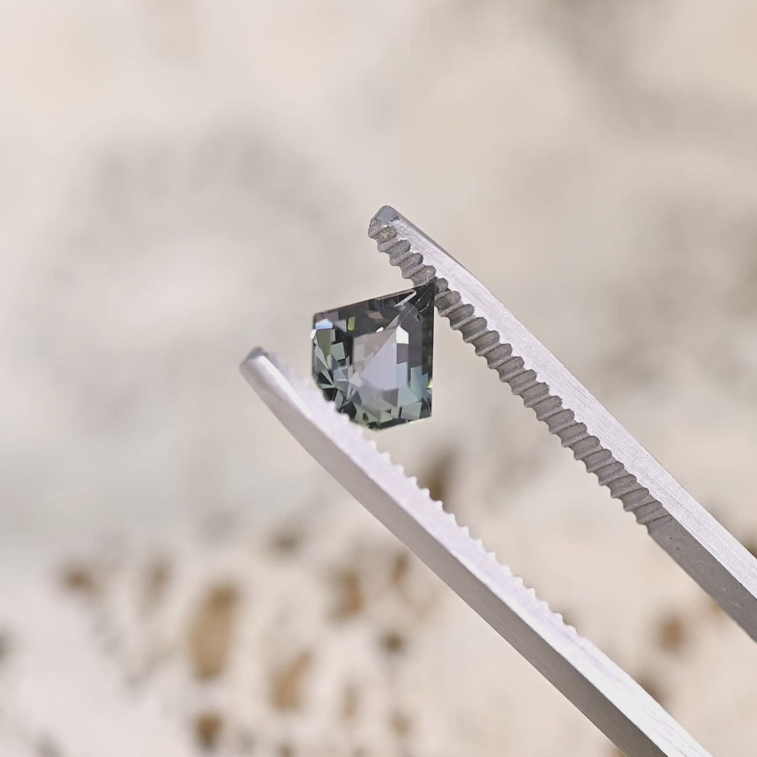 Close-up video of 1.36ct yellow green teal Tanzanite geometric shield held in tweezers, precision cut gemstone from Tanzania displaying brilliance, clarity and sharp angular faceting