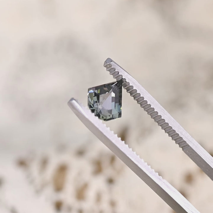 Close-up video of 1.36ct yellow green teal Tanzanite geometric shield held in tweezers, precision cut gemstone from Tanzania displaying brilliance, clarity and sharp angular faceting