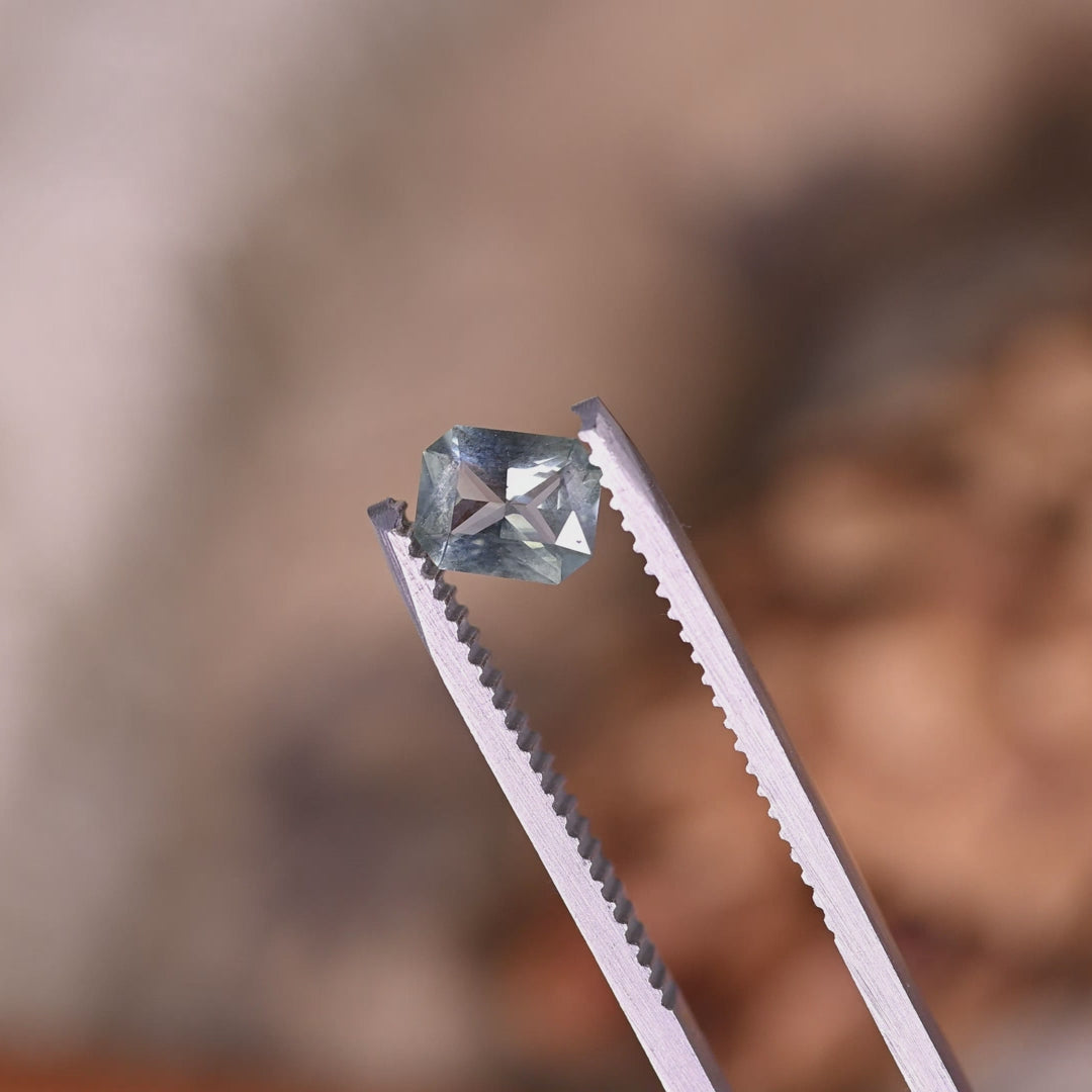 Video of 0.71ct Montana sapphire in tweezers rotating under light, teal blue green radiant mix cut showing sparkle and facet reflections