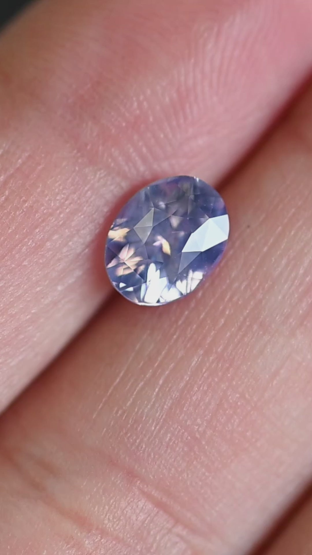 1.63ct opalescent pinkish purple sapphire rotating in hand, showing shifting lavender and rose flashes across the oval mix cut.