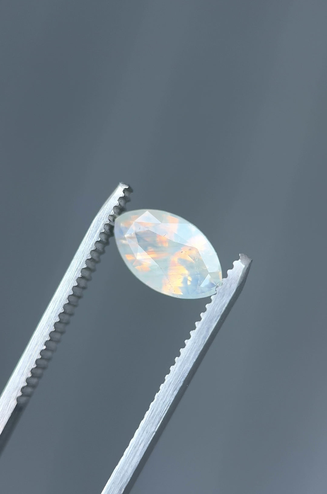 Macro video of 2.18CT opalescent peach and gray sapphire rotating in gemstone tweezers, revealing luminous shimmer and clarity in a precision marquise mixed cut, unheated sapphire from Ratnapura, Sri Lanka.