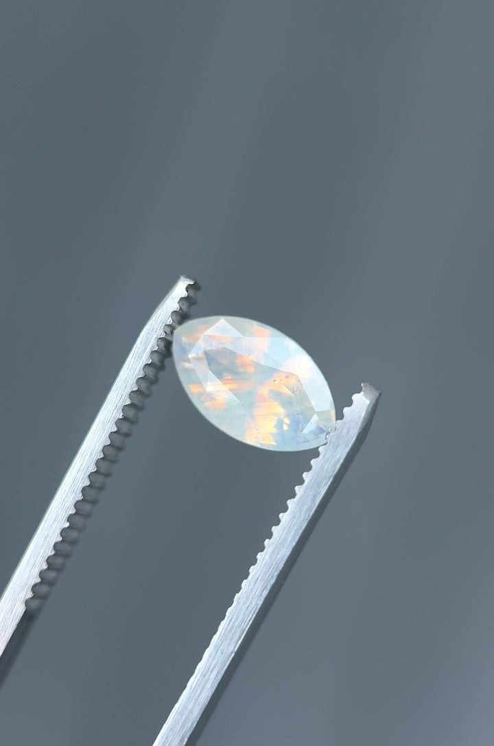 Macro video of 2.18CT opalescent peach and gray sapphire rotating in gemstone tweezers, revealing luminous shimmer and clarity in a precision marquise mixed cut, unheated sapphire from Ratnapura, Sri Lanka.