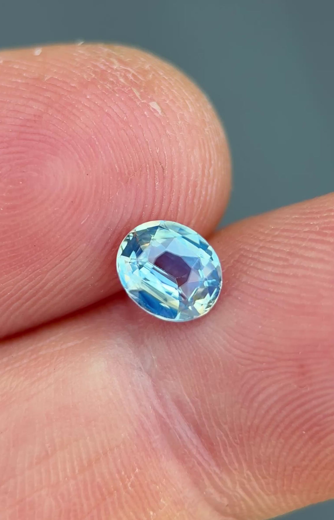 1.15ct opalescent powder blue sapphire rotating in hand, revealing soft sky-blue flashes and precision oval brilliance.