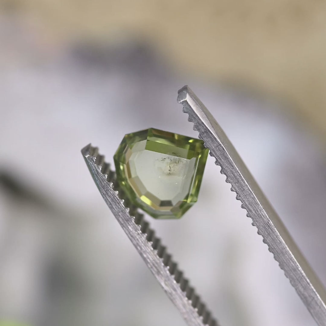 Video of a 1.75 carat Montana sapphire rotating in tweezers, revealing teal, yellow, and green color zoning, geometric step cut portrait pear shape, and untreated brilliance