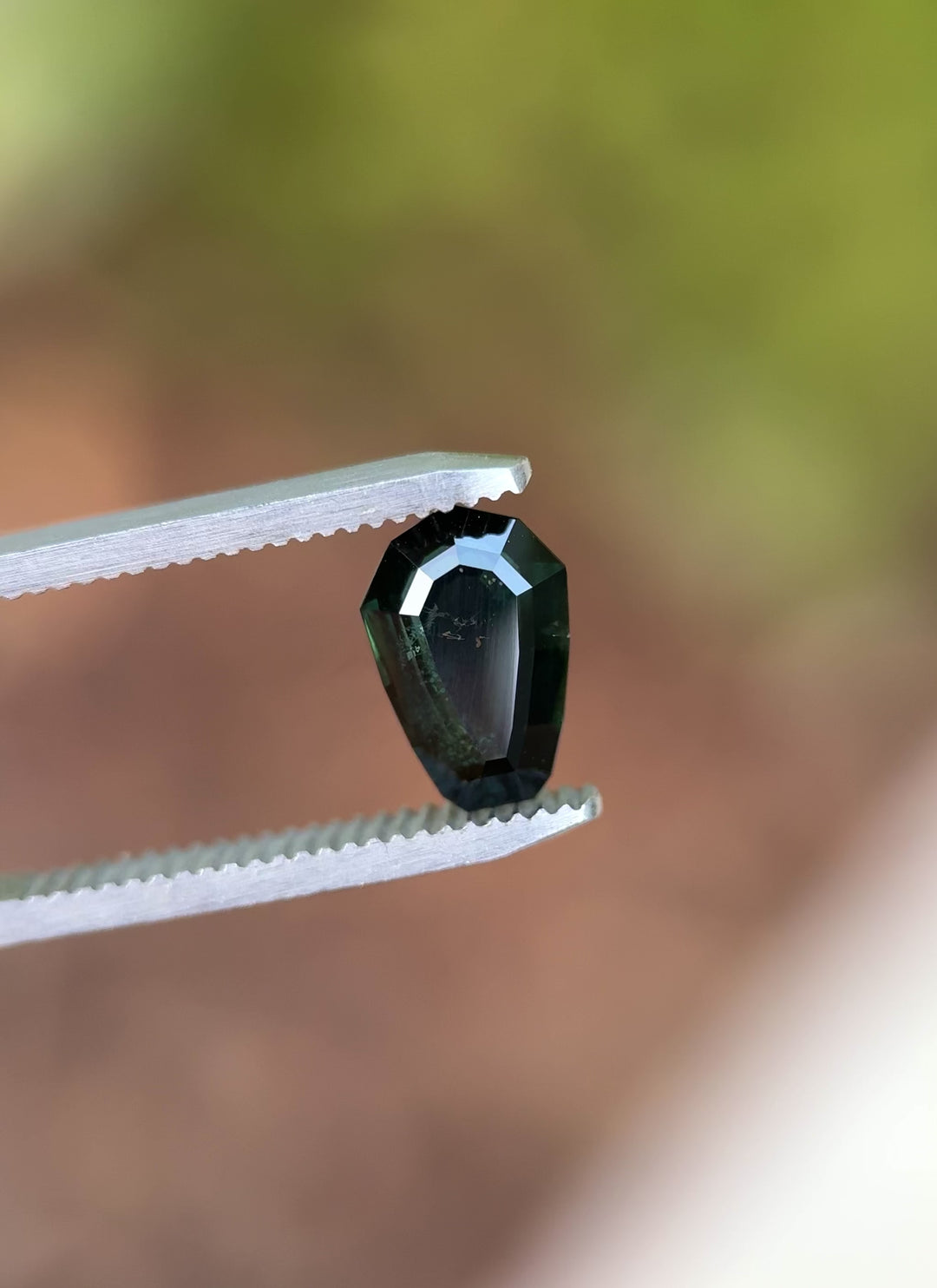 Video of a 3.07 carat untreated Nigerian sapphire with custom shield step cut, glistening with dark blue-green tones in natural lighting.