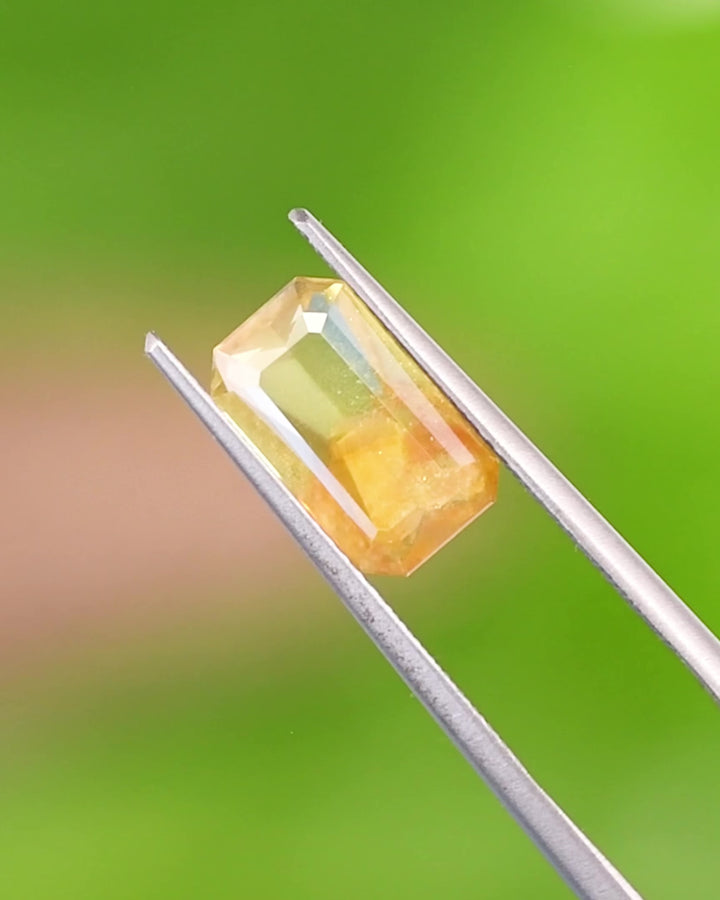 Close-up video of 2.74CT parti sapphire rotating in gemstone tweezers under natural light, capturing vivid color transitions from green to yellow and orange, and the precise geometry of its custom octagonal step cut, unheated sapphire from Umba River, Tanzania.
