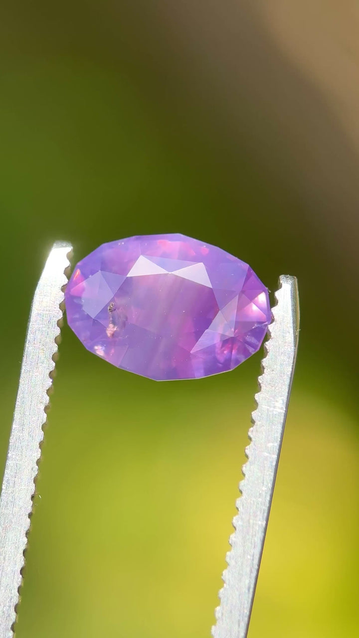 Natural Madagascar sapphire turning in tweezers, showcasing modified oval brilliant faceting and luminous pastel pink color.