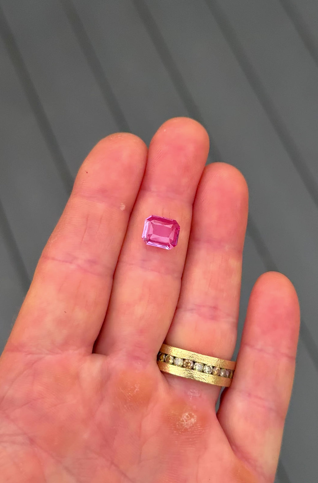 Close-up video of 3.01 carat pink sapphire shown on fingertips under natural light, highlighting flashes of soft rose and vivid magenta in the custom octagonal portrait cut, untreated gemstone from Madagascar.