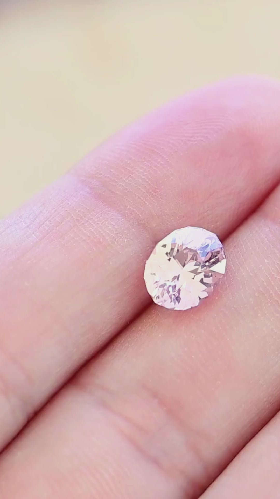 Untreated 2.50 carat peach blush pink sapphire moving on a hand, revealing its soft pastel color and flashes of pink, peach and subtle lavender through the geometric oval brilliant facets.