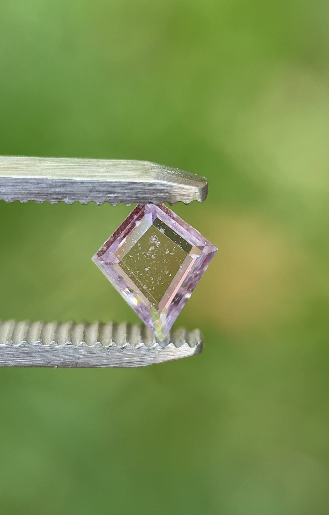 0.97ct pastel purple-pink sapphire from Colombia shown in hand under natural light, revealing clarity, precision step cut, and flat kite form.
