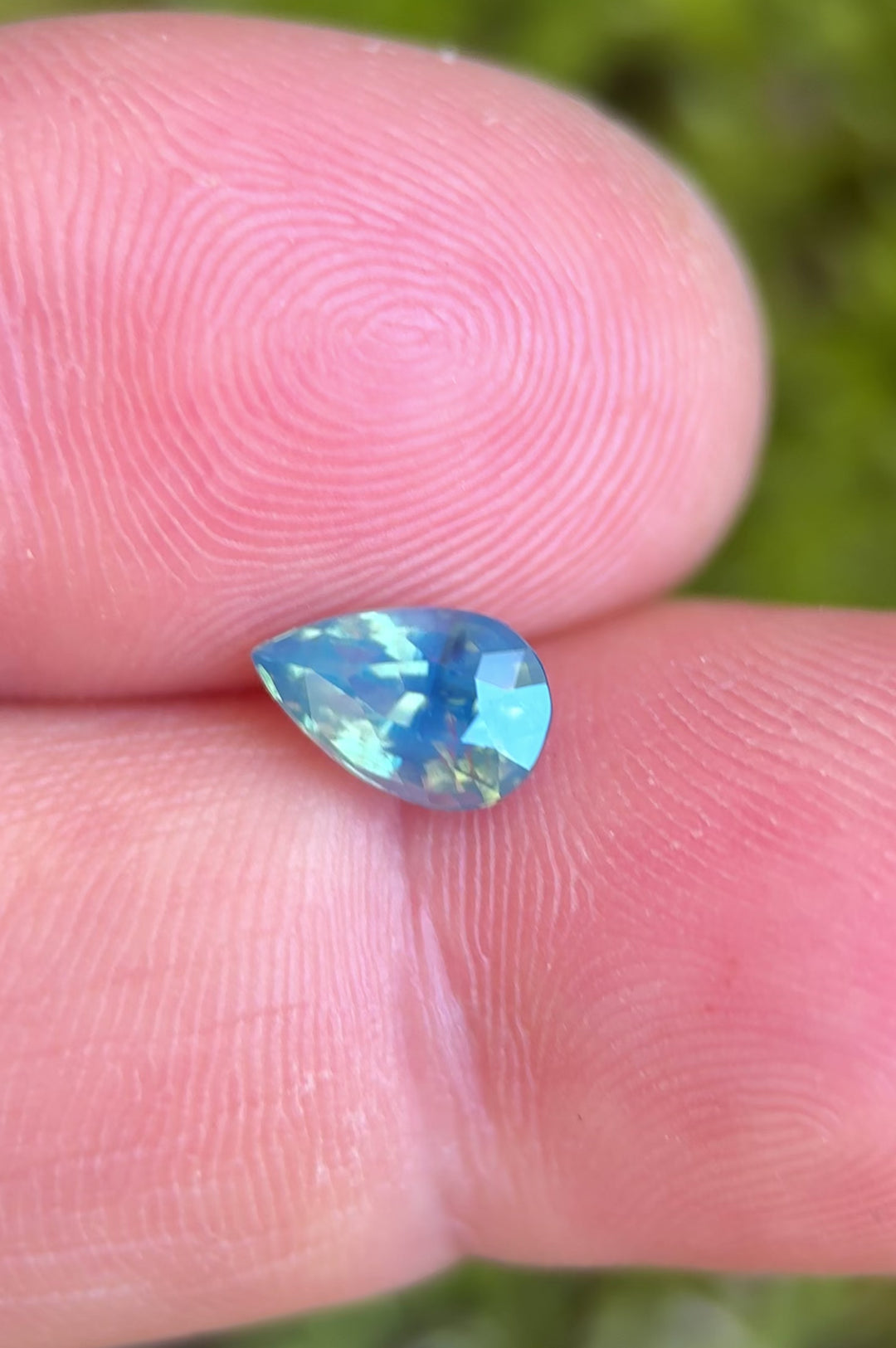 1.50ct opalescent teal blue green sapphire rotating in hand, revealing shifting oceanic tones and lively pear-cut brilliance.