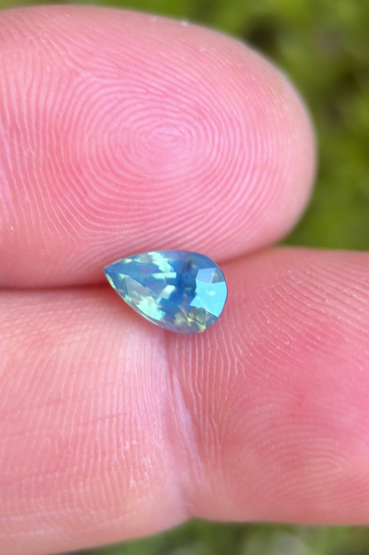 1.50ct opalescent teal blue green sapphire rotating in hand, revealing shifting oceanic tones and lively pear-cut brilliance.