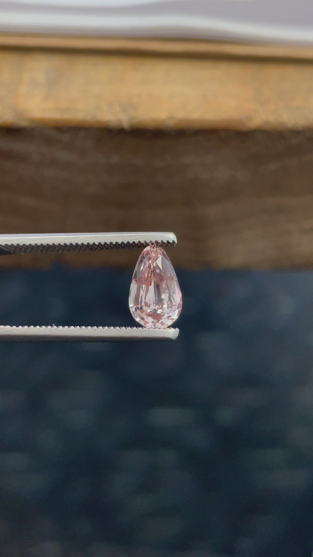 A 2.45-carat pastel champagne and peach sapphire rotates on display, showcasing its custom brilliant teardrop cut. The video captures the full 360-degree view of the gem, allowing light to interact with the facets and reveal the stone's natural beauty. Originating from Sri Lanka, the untreated sapphire has dimensions of 10.12mm by 6.40mm by 4.70mm.