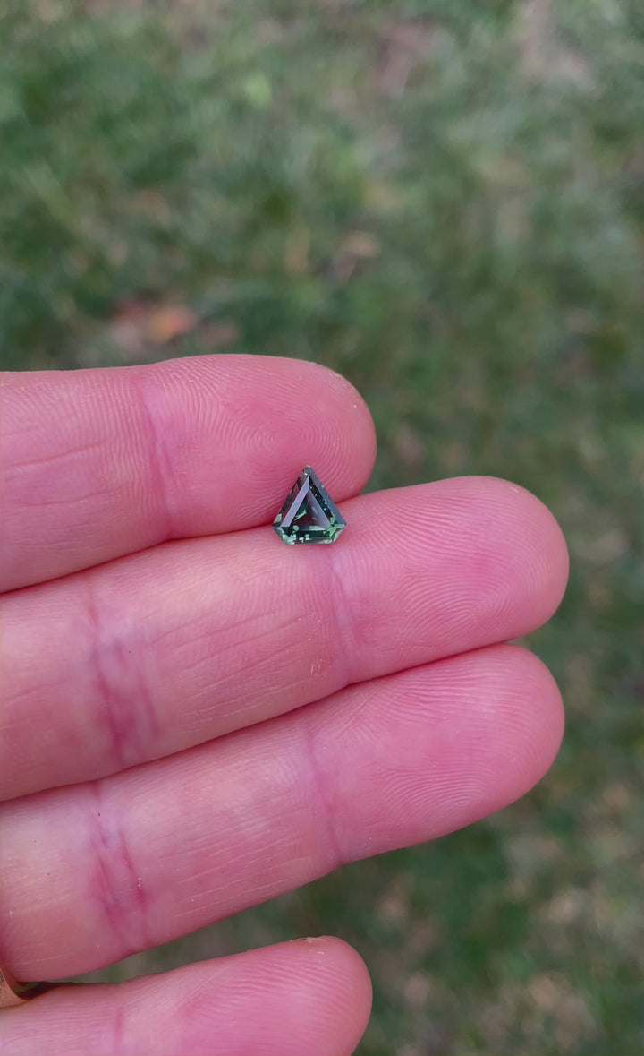 Video of a 1.57ct opalescent yellow-teal shield sapphire, rotating to display its step-cut facets and color variations under natural lighting.