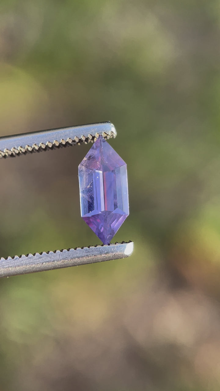 A mesmerizing 1.01-carat royal purple and pink sapphire in a hexagon step cut, reflecting light beautifully as it moves in metal tweezers.