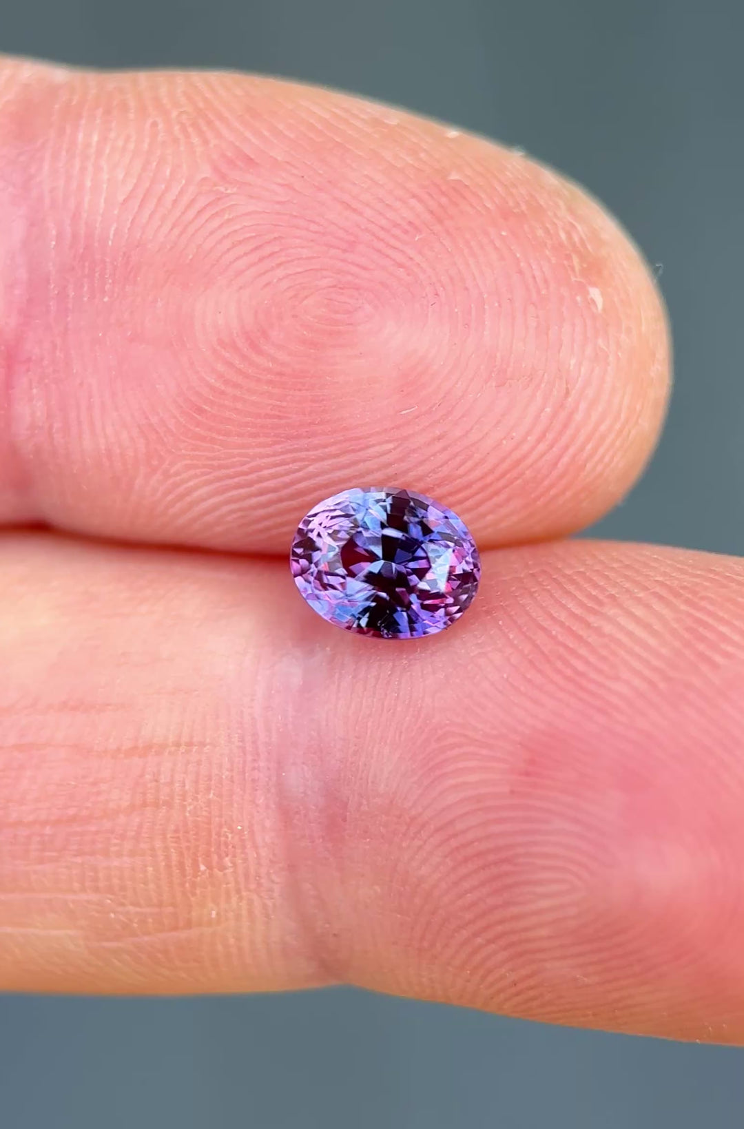 Precision oval cut sapphire resting on fingertips, showing saturated pink and purple tones with exceptional brilliance.