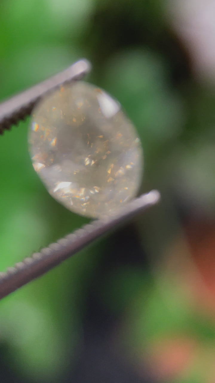 A handheld tweezer view of the 2.71-carat oval modified brilliant diamond, showing its size, clarity, and beautiful color transitions in movement.