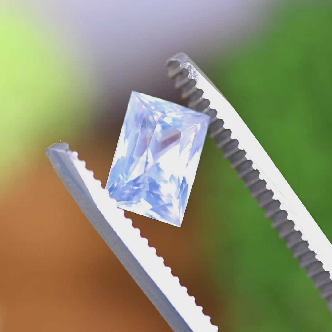 Rotating loose opalescent white to colorless sapphire from Ratnapura, Sri Lanka held in tweezers, showing the clean geometry and shifting glow of the elongated princess cut.