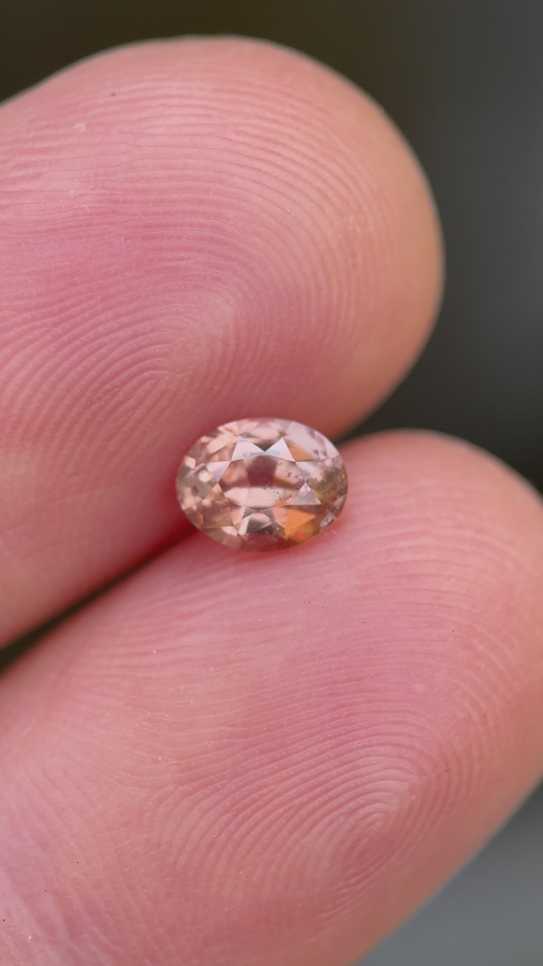 Rotating hand-held video of oval mix cut 0.95ct peach pink sapphire highlighting internal clarity, surface brilliance, and changing hues under daylight.