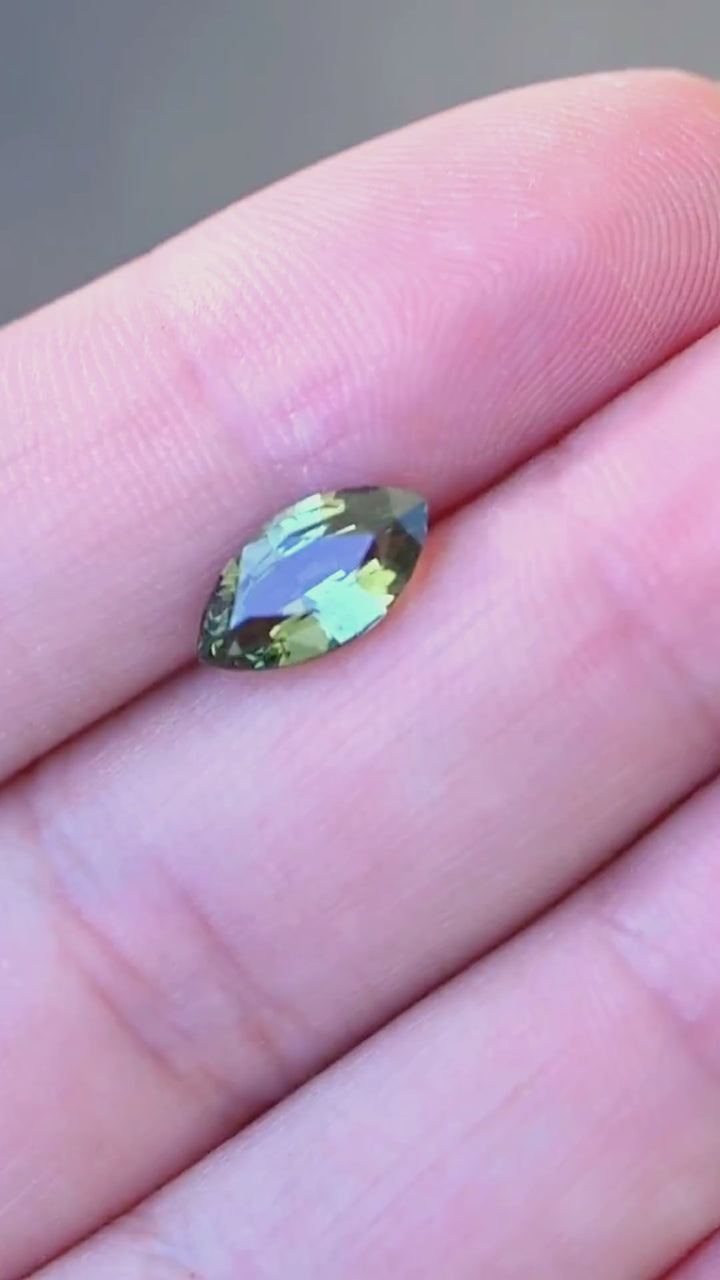 Explore a 2.03 carat teal blue yellow parti sapphire from Diego, Madagascar, displayed on the hand for scale. This heated natural sapphire features an unusual combination of forest green, turquoise blue and golden-yellow coloration, with a custom faceted cut suited to bespoke engagement rings and fine jewelry.