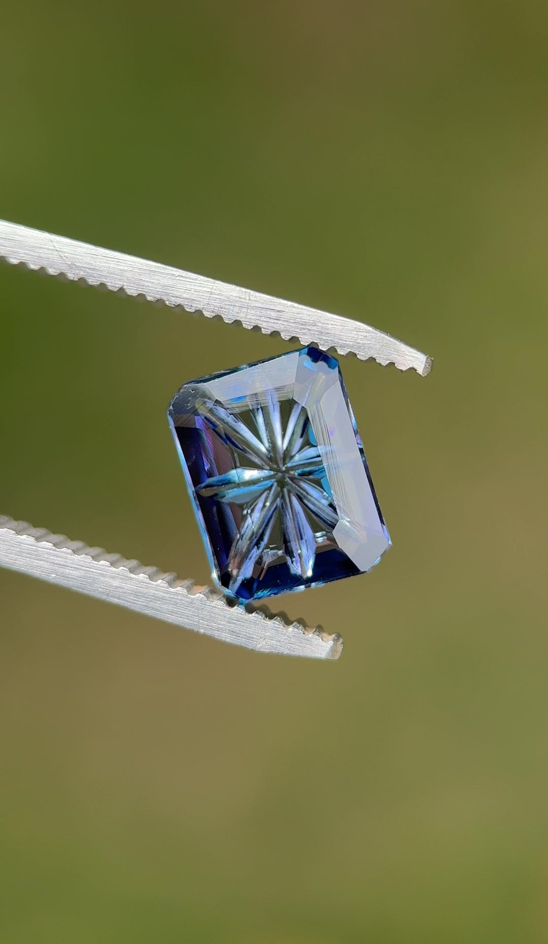 Close-up video of a natural 2.99ct Tanzanite displaying its violet, teal, and blue color shift while being moved in tweezers, revealing the depth of the concave portrait cut and untreated clarity.