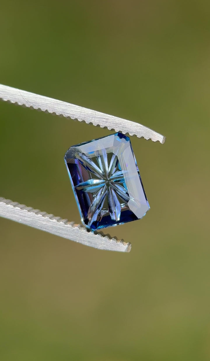 Close-up video of a natural 2.99ct Tanzanite displaying its violet, teal, and blue color shift while being moved in tweezers, revealing the depth of the concave portrait cut and untreated clarity.