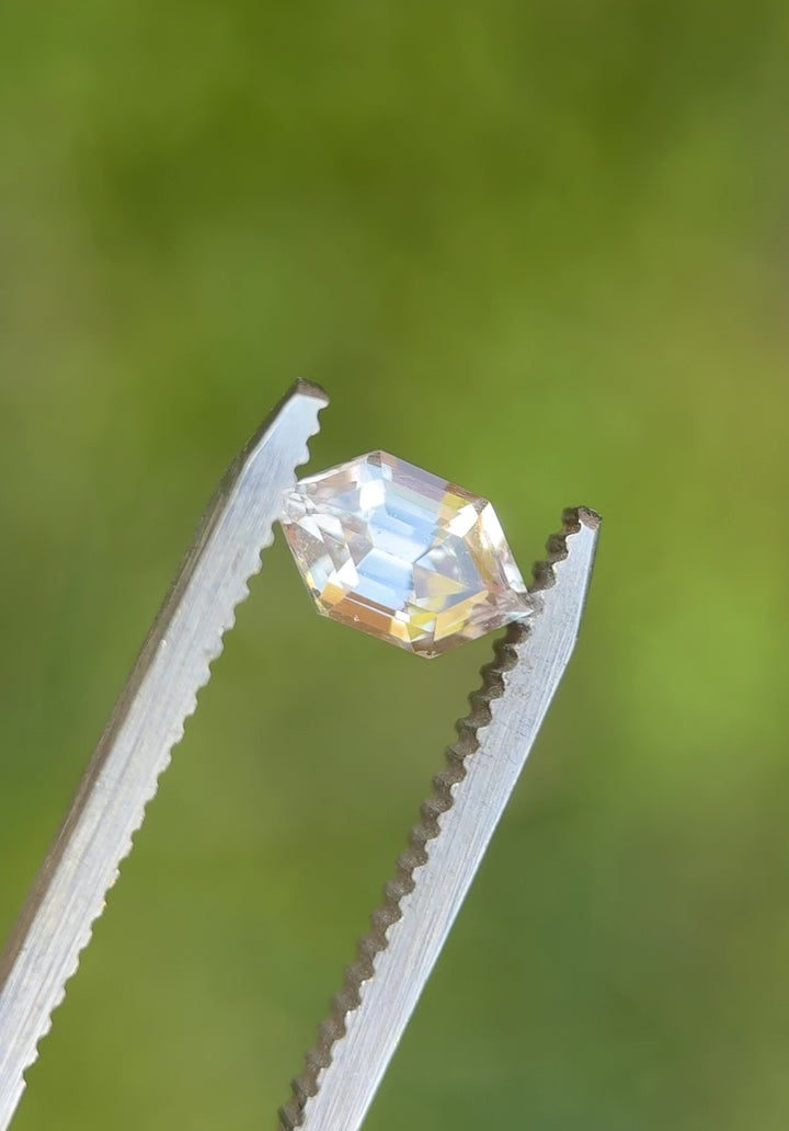 Hexagon step cut sapphire rotating in tweezers showing mirror-like facets and subtle pale yellow gray tones.