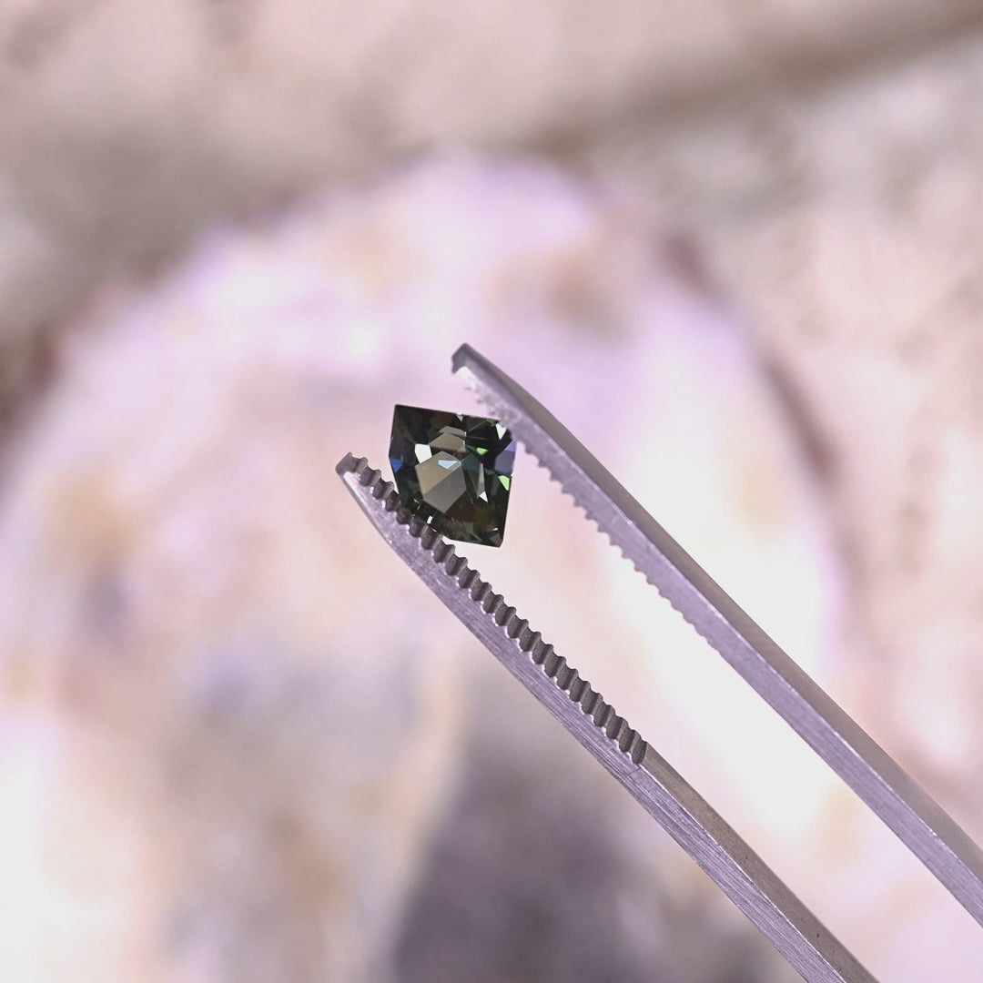 Rotating loose teal, yellow, and green tanzanite from Merelani Hills, Tanzania in tweezers, revealing the brilliance and color variation of the geometric shield mix cut.
