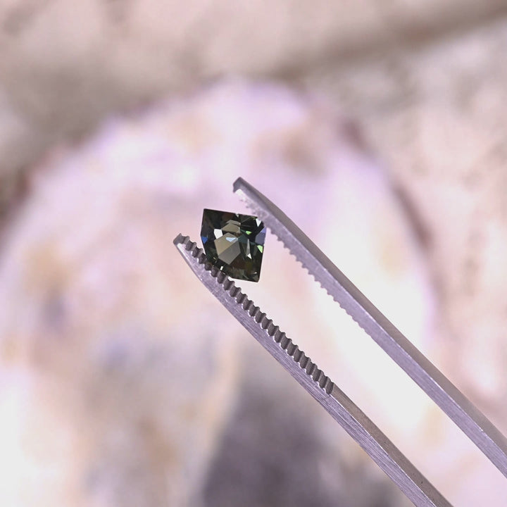 Rotating loose teal, yellow, and green tanzanite from Merelani Hills, Tanzania in tweezers, revealing the brilliance and color variation of the geometric shield mix cut.