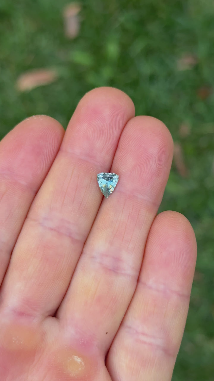 Handheld video of 1.08 carat sapphire in shield shape under natural light, highlighting the custom cut and blue-teal hues.