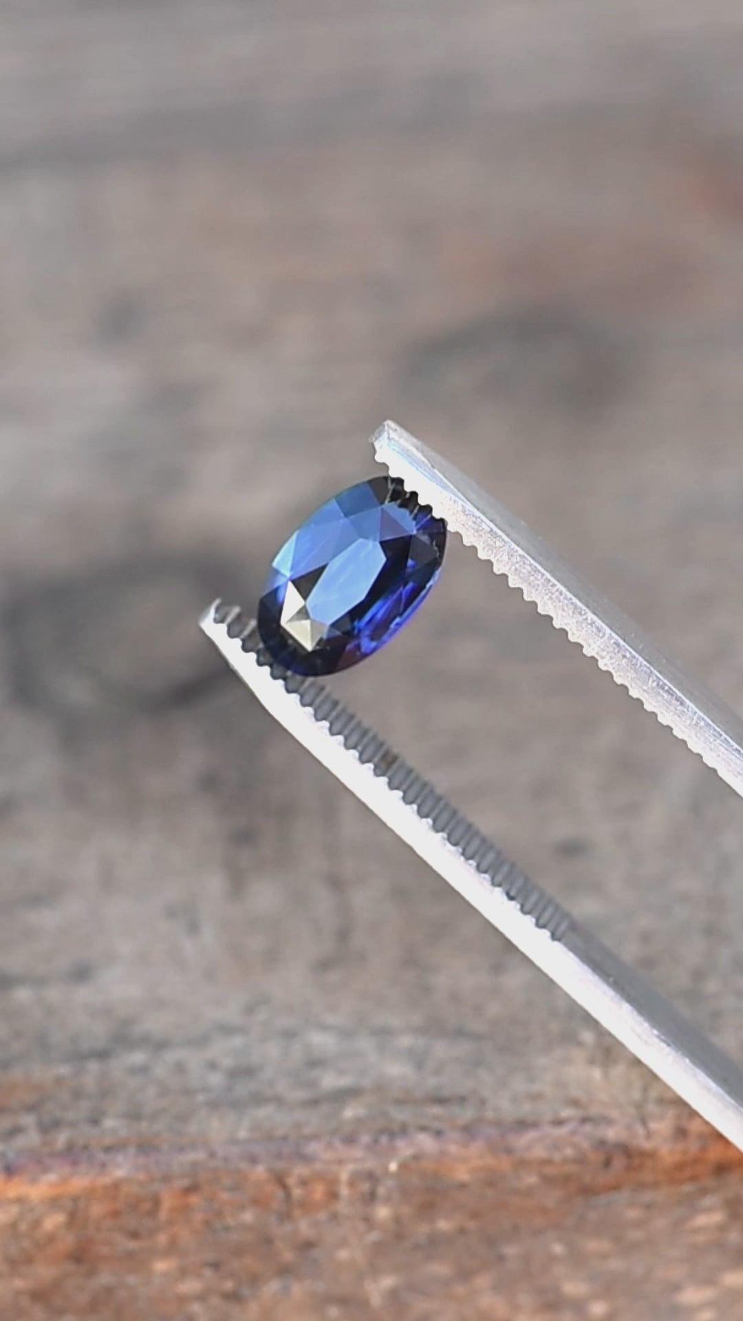 2.02ct deep blue elongated moval cut sapphire from madagascar rotating in gem tweezers under natural light.