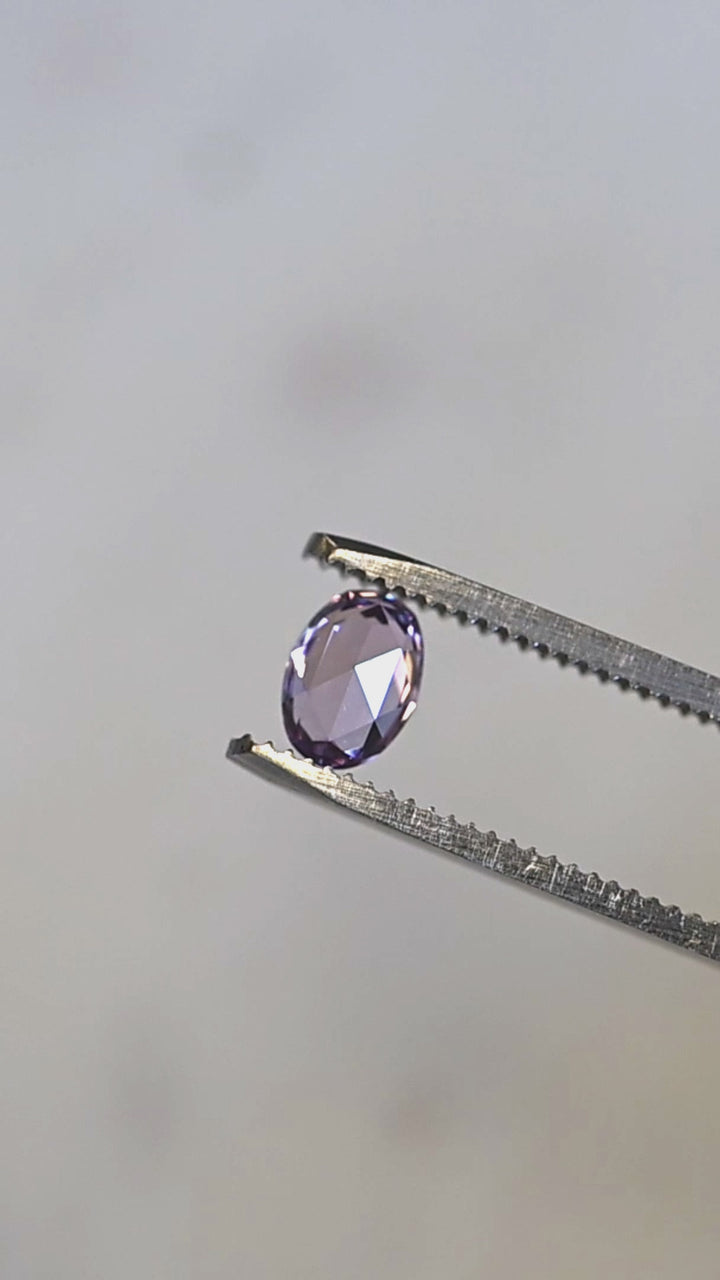 Natural Madagascar sapphire turning in tweezers, showcasing rose cut faceting and subtle lavender pink color shifts in natural light.