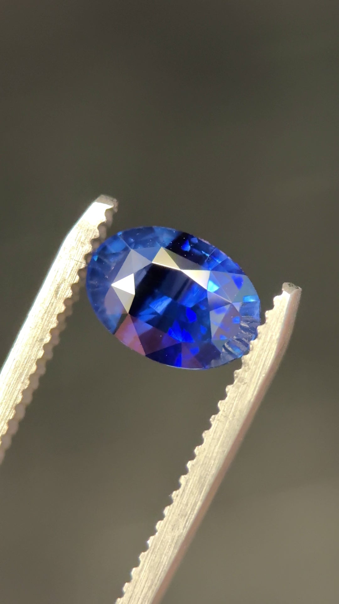 Video of a 2.56-carat striated royal blue parti sapphire from Diego, Madagascar, rotating in tweezers under natural light to reveal color zoning, brilliance, and precision oval mixed cut facets, untreated.