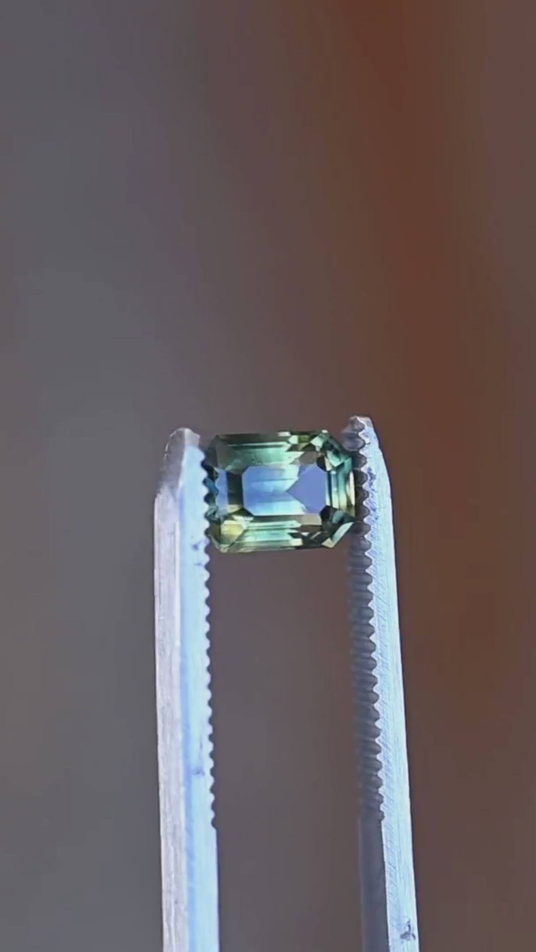A close-up presentation of a 2.16ct untreated yellow teal green parti sapphire from Diego, Madagascar. Its elongated octagonal step cut reveals distinct color zoning and layered geometric reflections.
