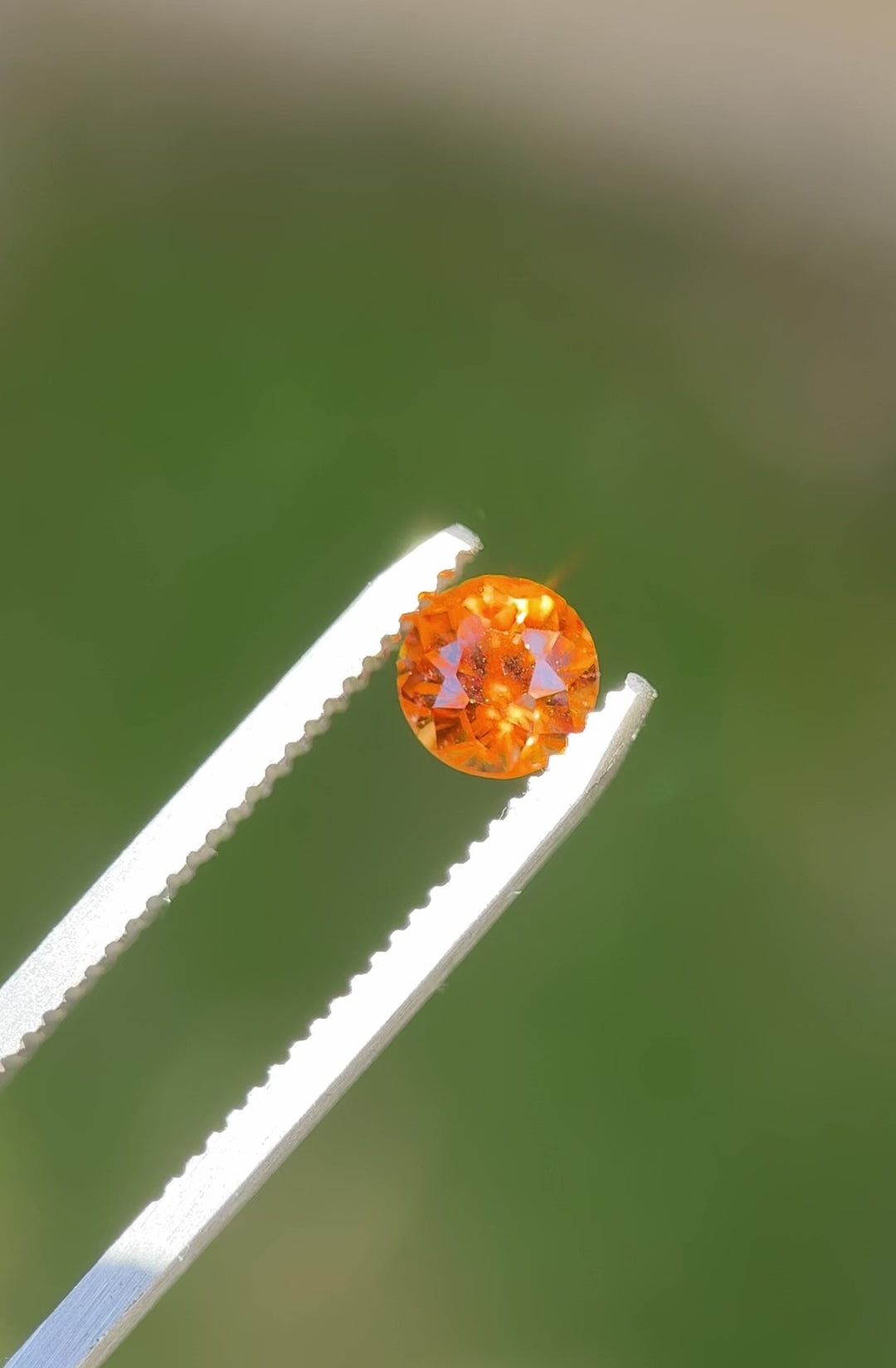 Hessonite garnet held in tweezers, tilting to reveal golden hues and internal brilliance under sunlight