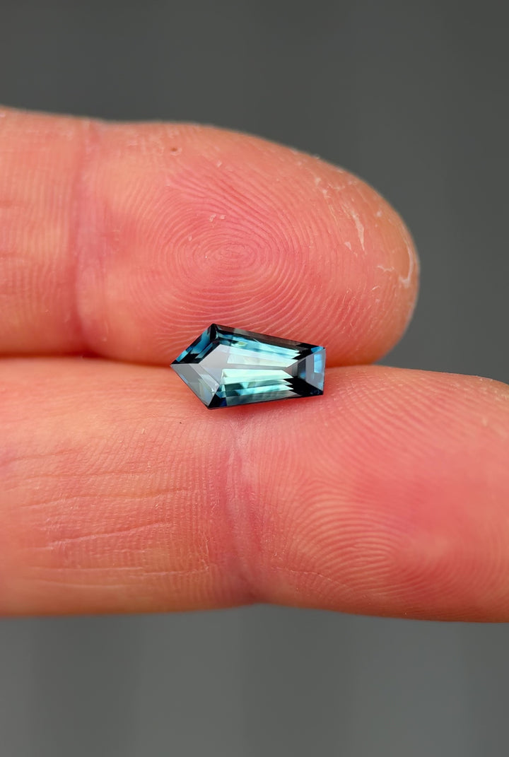 Handheld video of a 2.11-carat teal blue parti sapphire in elongated shield step cut, shifting in natural light to reveal banded parti colors and crisp faceting.
