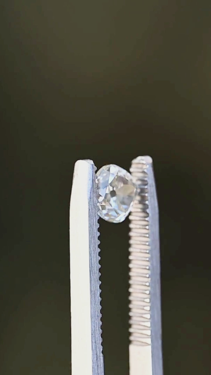 White antique-style cushion diamond slowly turning in tweezers under shaded natural light, highlighting crisp facet definition and subtle, even brilliance.