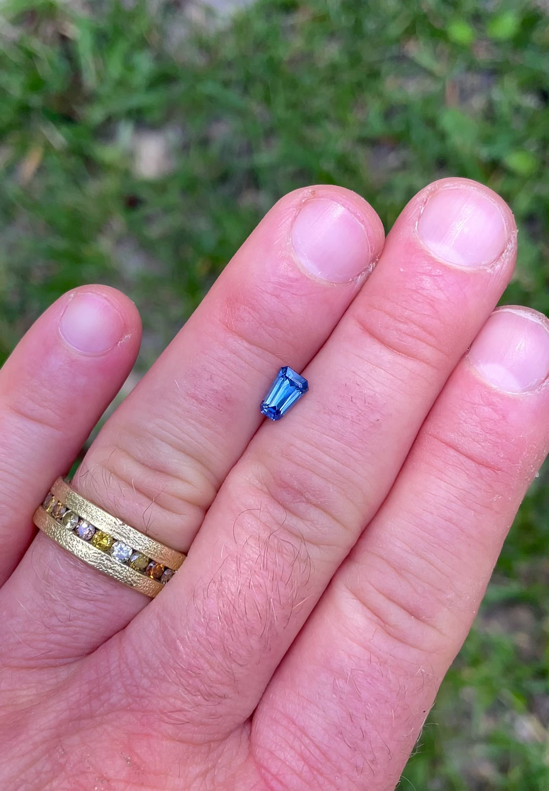 1.20 carat heated blue sapphire from El Dorado Bar, Montana shown on fingertips in natural light, revealing tapered shield step cut and intense blue brilliance.