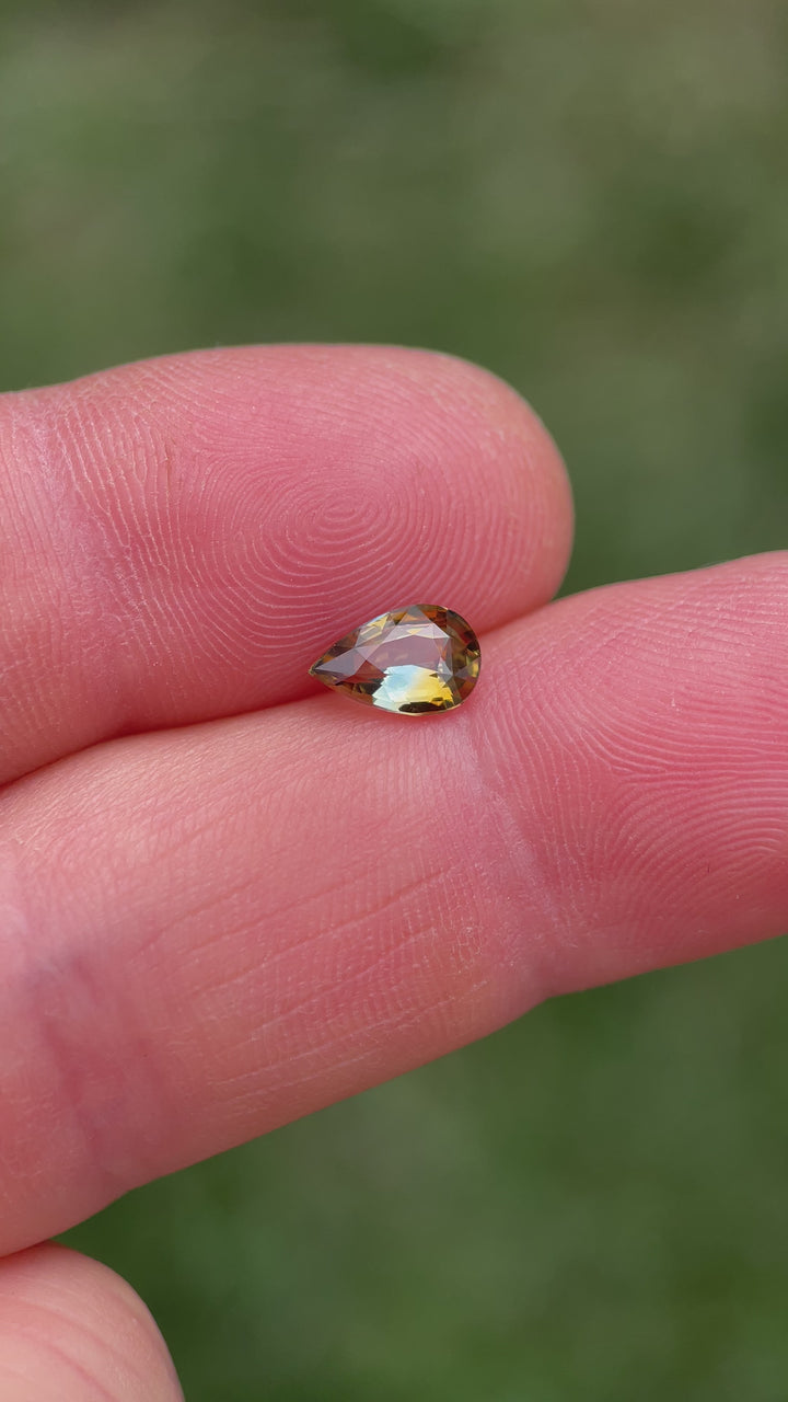 Dynamic video of a 1.00-carat bi-color sapphire in pear cut, revealing shifting tones of brown and bluish green under changing light angles.