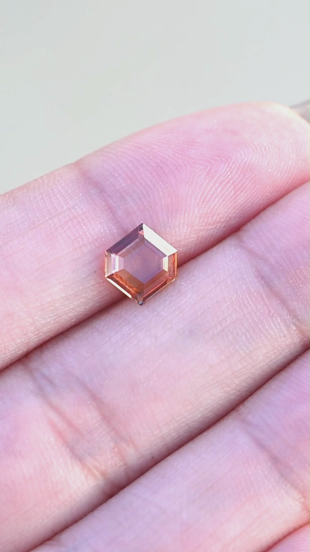 Natural orange portrait cut sapphire held in fingertips rotating under natural light.