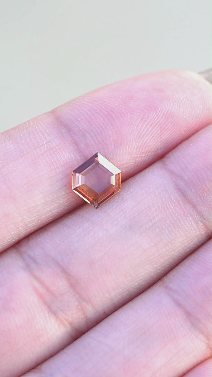 Natural orange portrait cut sapphire held in fingertips rotating under natural light.