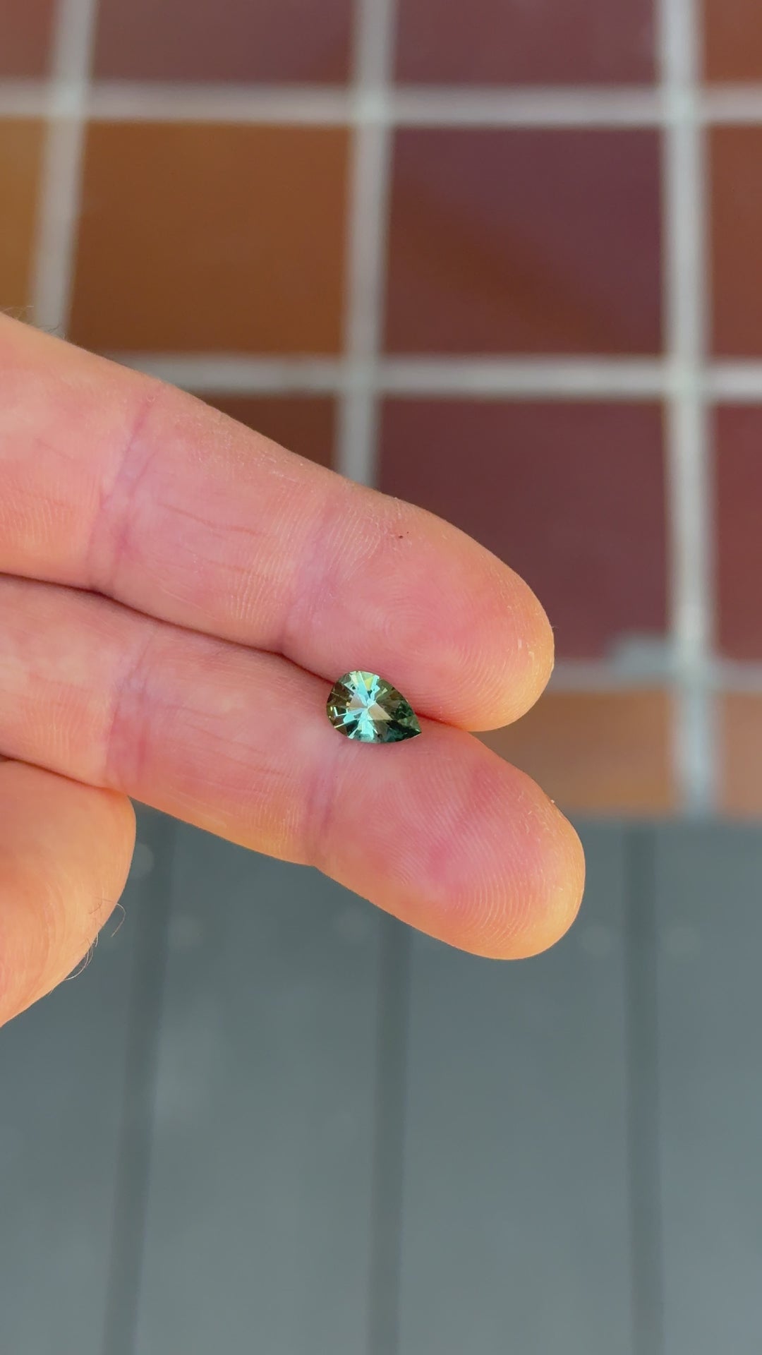 Close-up video of a 1.34 carat heated Montana sapphire turning under natural light, showcasing lagoon teal green color play, step cut facets, and shield shape symmetry.