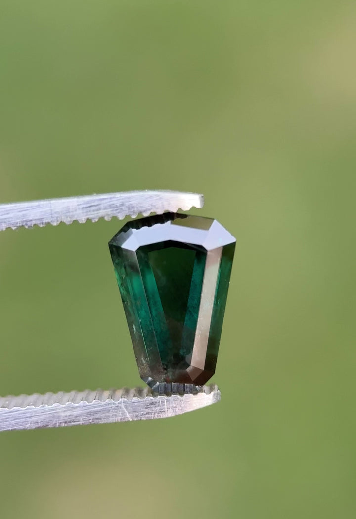 A close-up video of a 3.65ct untreated Kenyan sapphire held by tweezers. The vibrant teal and blue gem sparkles with clarity against a softly blurred, peach-toned background.