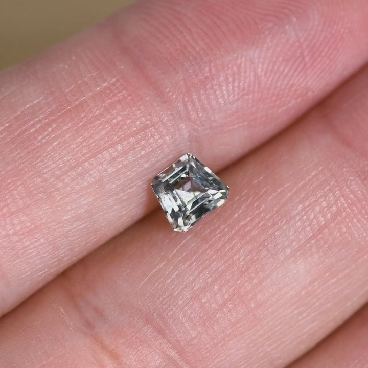 0.82ct seafoam Montana sapphire rotated in hand, showing shifting mint and pale blue tones with mirrored flashes from the step-cut facets