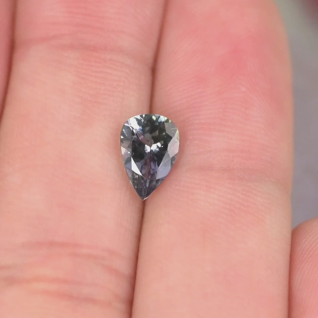 Close-up video of 1.10ct violet teal pear Tanzanite held on hand, precision modified brilliant faceting displaying bright starburst reflections and natural Tanzania color play