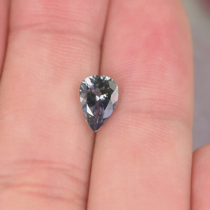 Close-up video of 1.10ct violet teal pear Tanzanite held on hand, precision modified brilliant faceting displaying bright starburst reflections and natural Tanzania color play