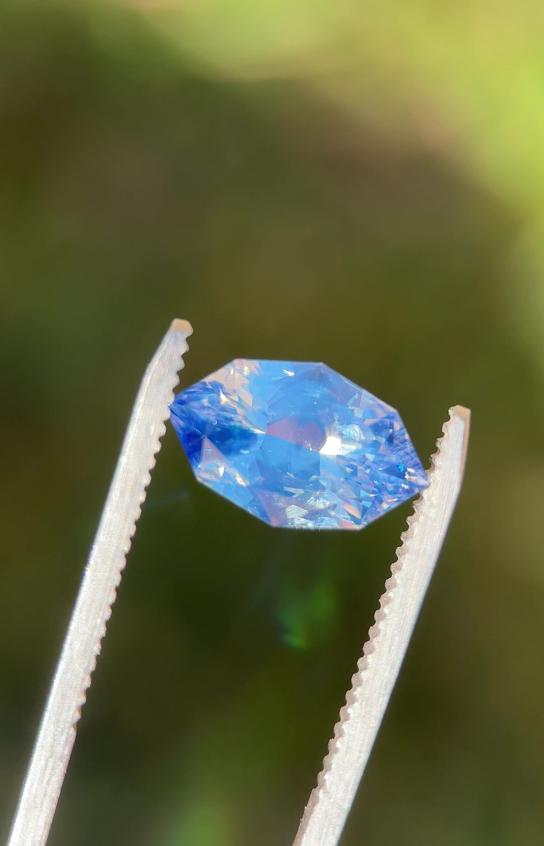 Video of 5.00CT blue white parti sapphire rotating in gemstone tweezers, showing shifting light play, intricate facet reflections, and color zoning of the precision custom marquise mixed cut, unheated sapphire from Sakaraha, Madagascar.